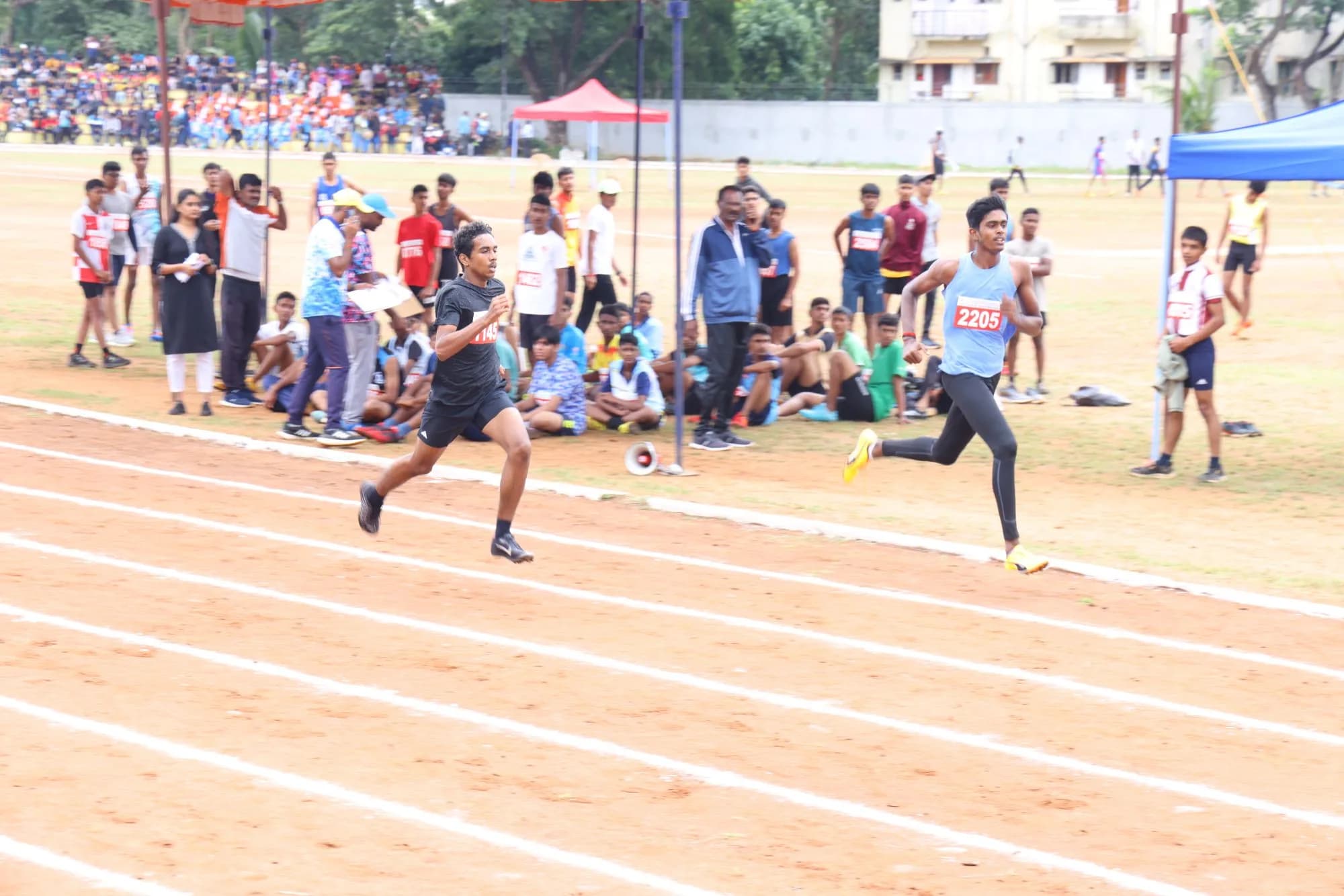 The closing stretch of a sprint on the campus track, watched from a full gallery — CBSE Cluster VIII Athletics Meet, 2024.