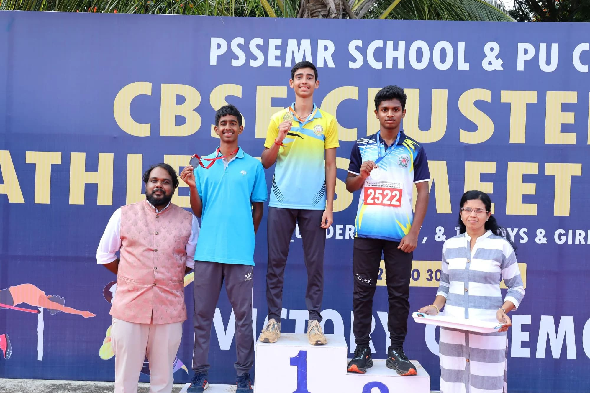 Three medallists on the victory podium with school staff, in front of the championship banner.