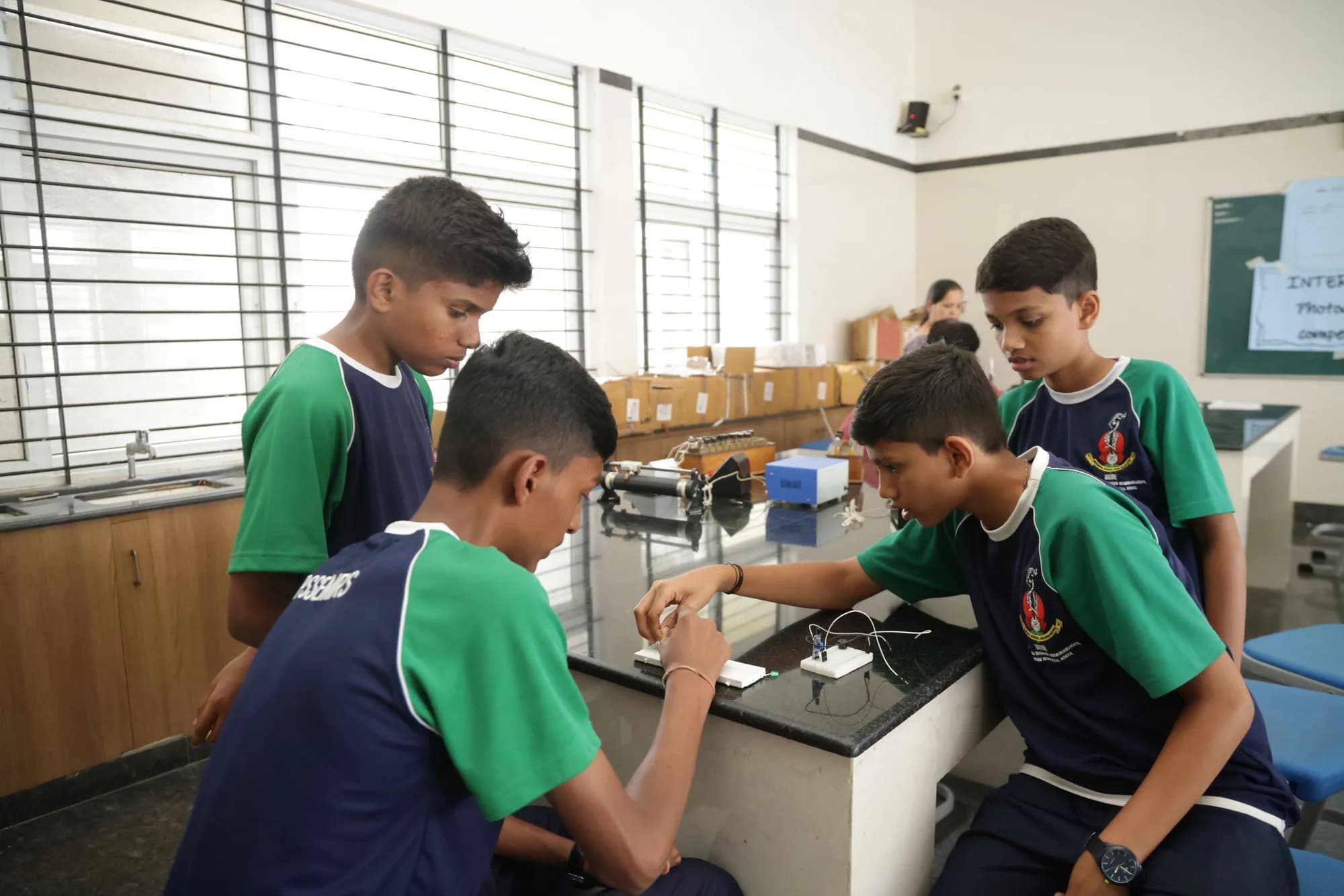 Four students building a breadboard circuit at a PSSEMR School physics bench
