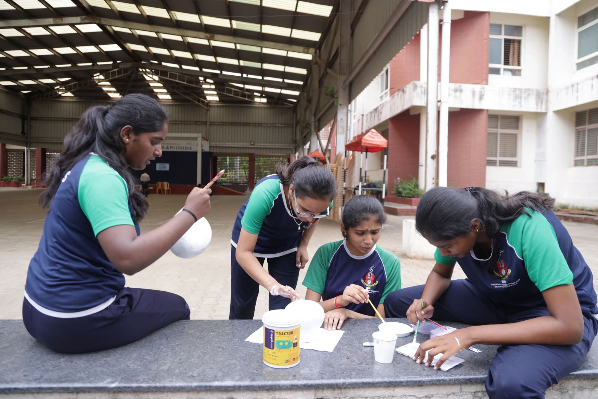 Four girls painting craft pieces under the assembly shed at PSSEMR School