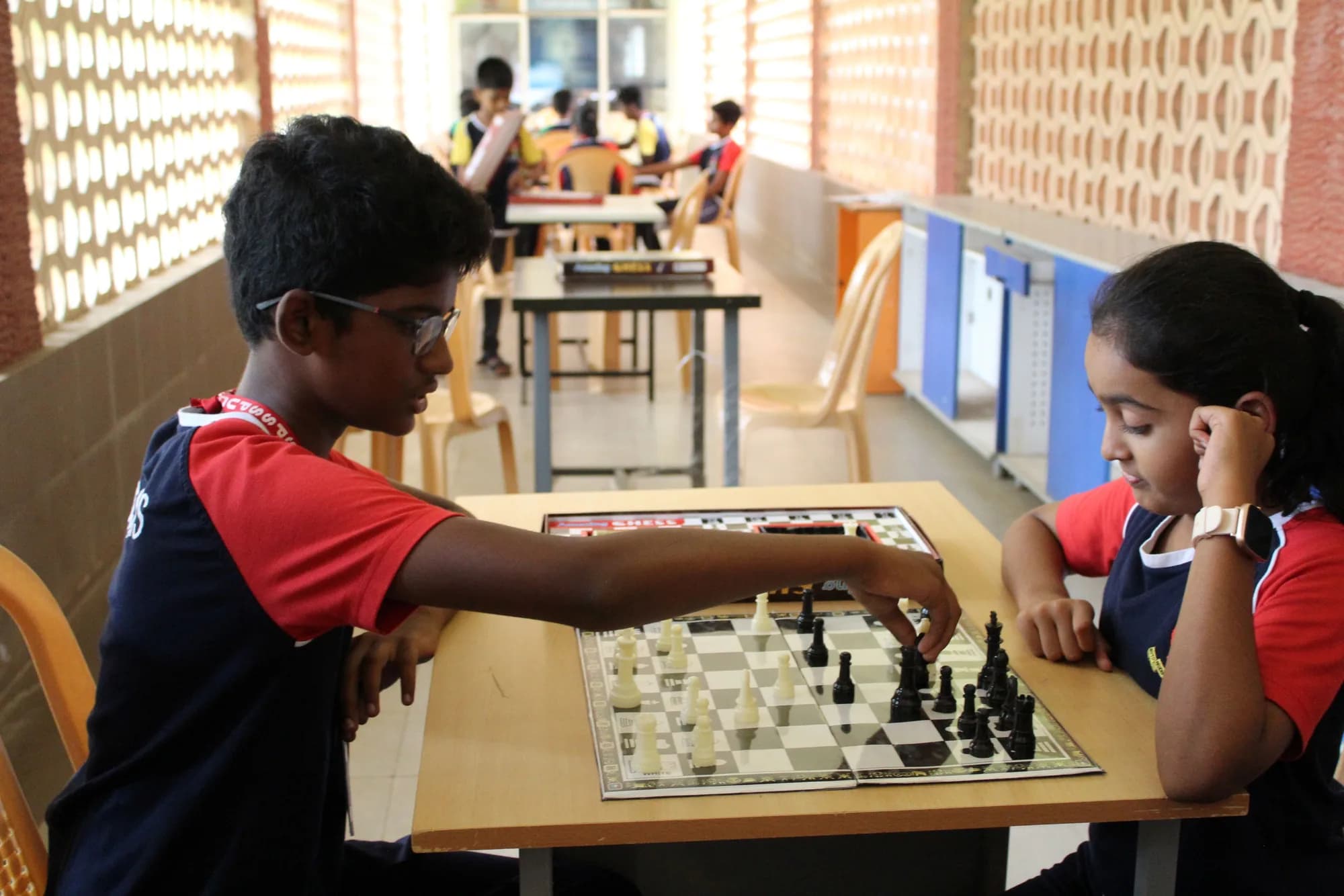 A boy and a girl playing chess in an open corridor at PSSEMR School