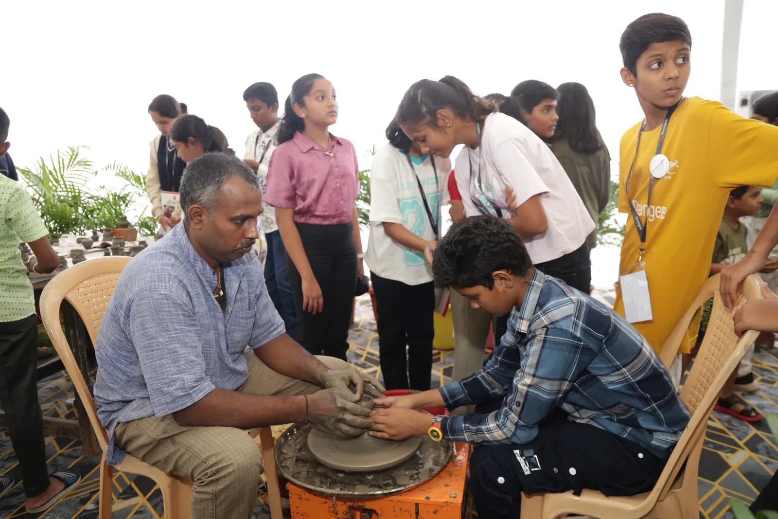 A potter guiding a student at the wheel in the Experience Zone