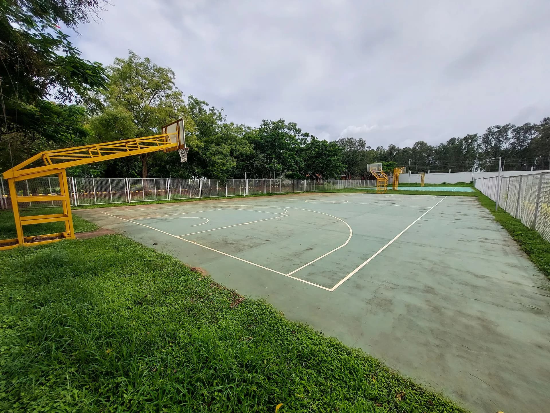 Outdoor basketball court at PSSEMR School, with yellow hoops and a chain-link fence