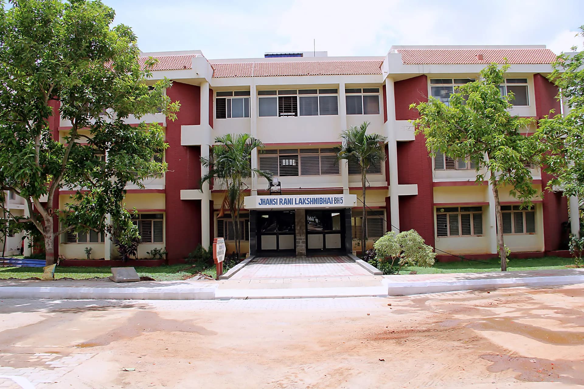 PSSEMR School hostel block with a tiled roof behind palm and mango trees