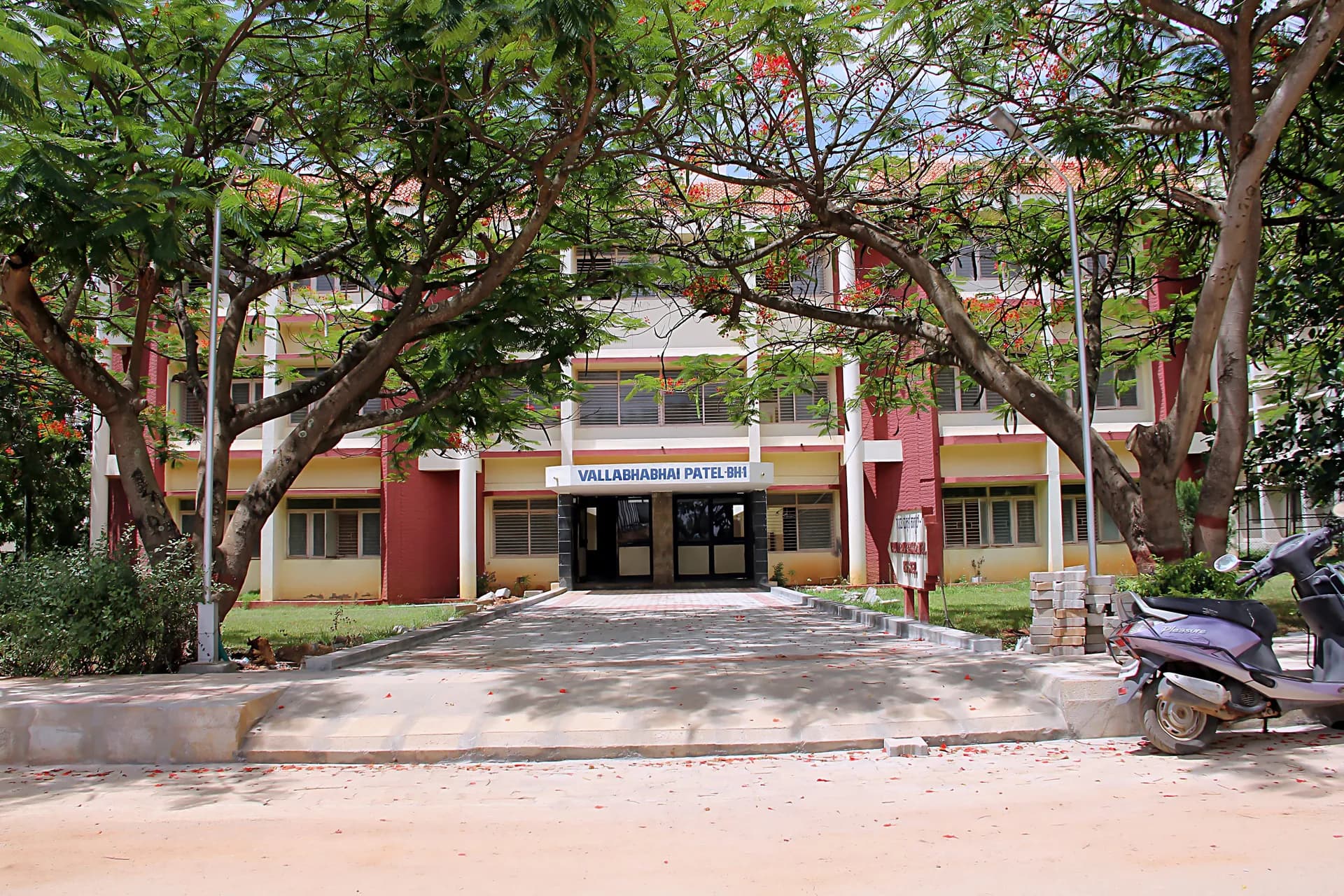 Three-storey boys' hostel block at PSSEMR School, framed by flowering gulmohar trees