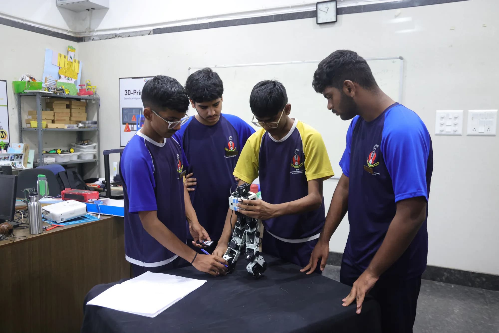 Four students working on a robot in the design lab at PSSEMR School, beside a 3D printer