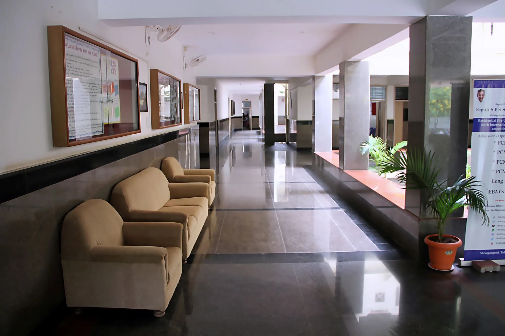 Long polished corridor at PSSEMR School with display boards, seating and potted palms