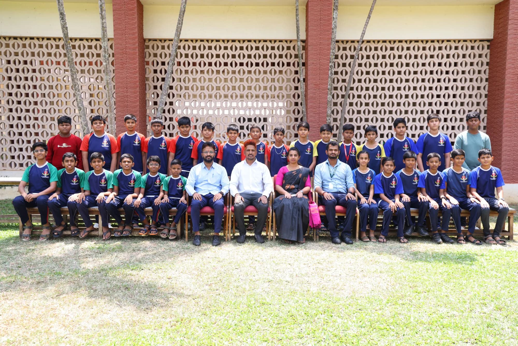 Boys in PSSEMR School house sports kit with staff, before a perforated screen wall
