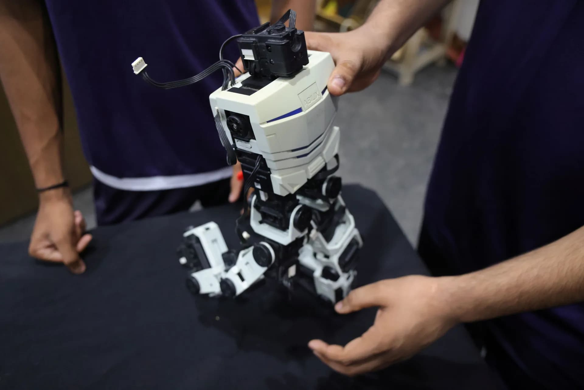 Two pairs of hands steadying a white humanoid robot on a workbench