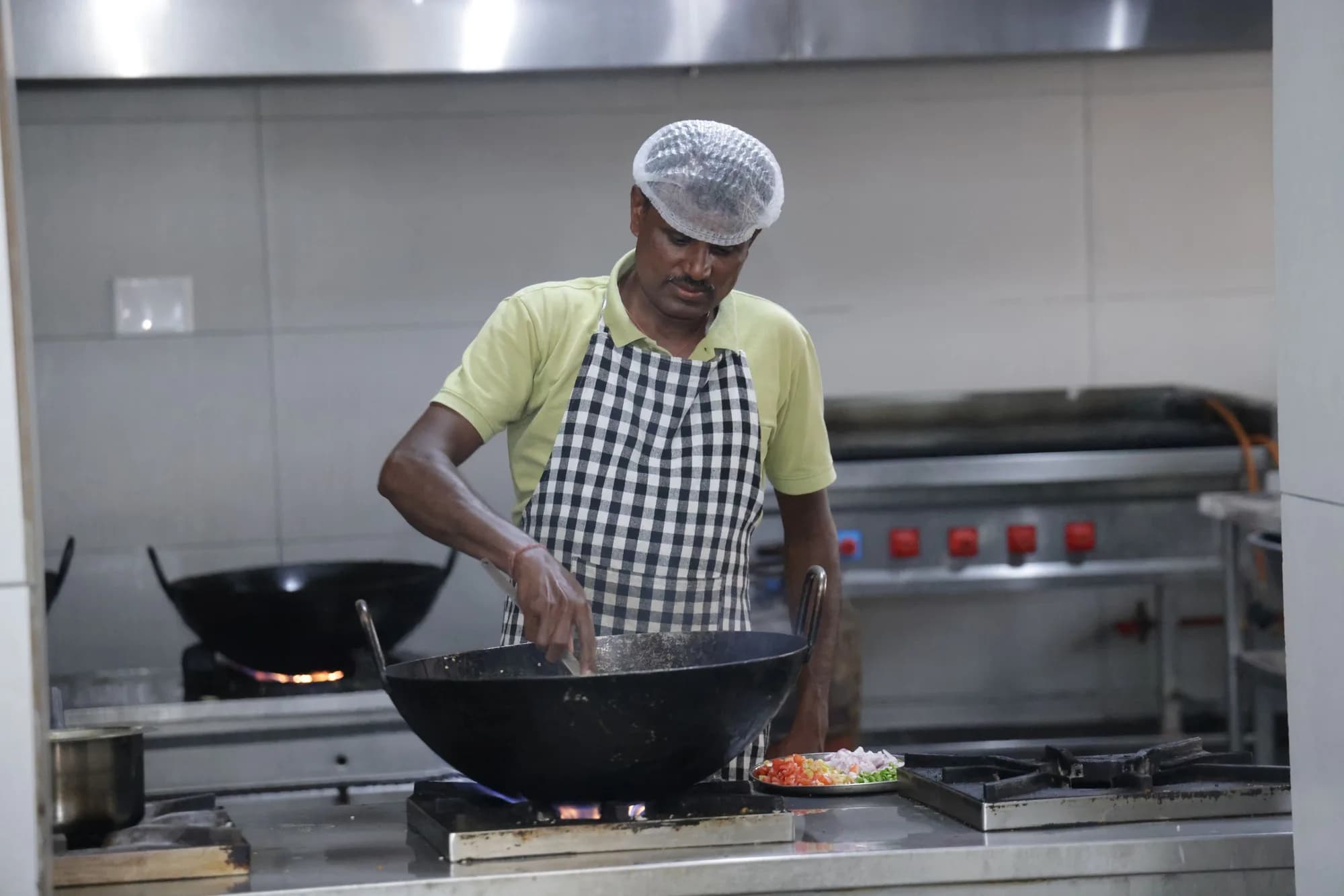 A cook stirring a large kadai over a gas range in the PSSEMR School kitchen