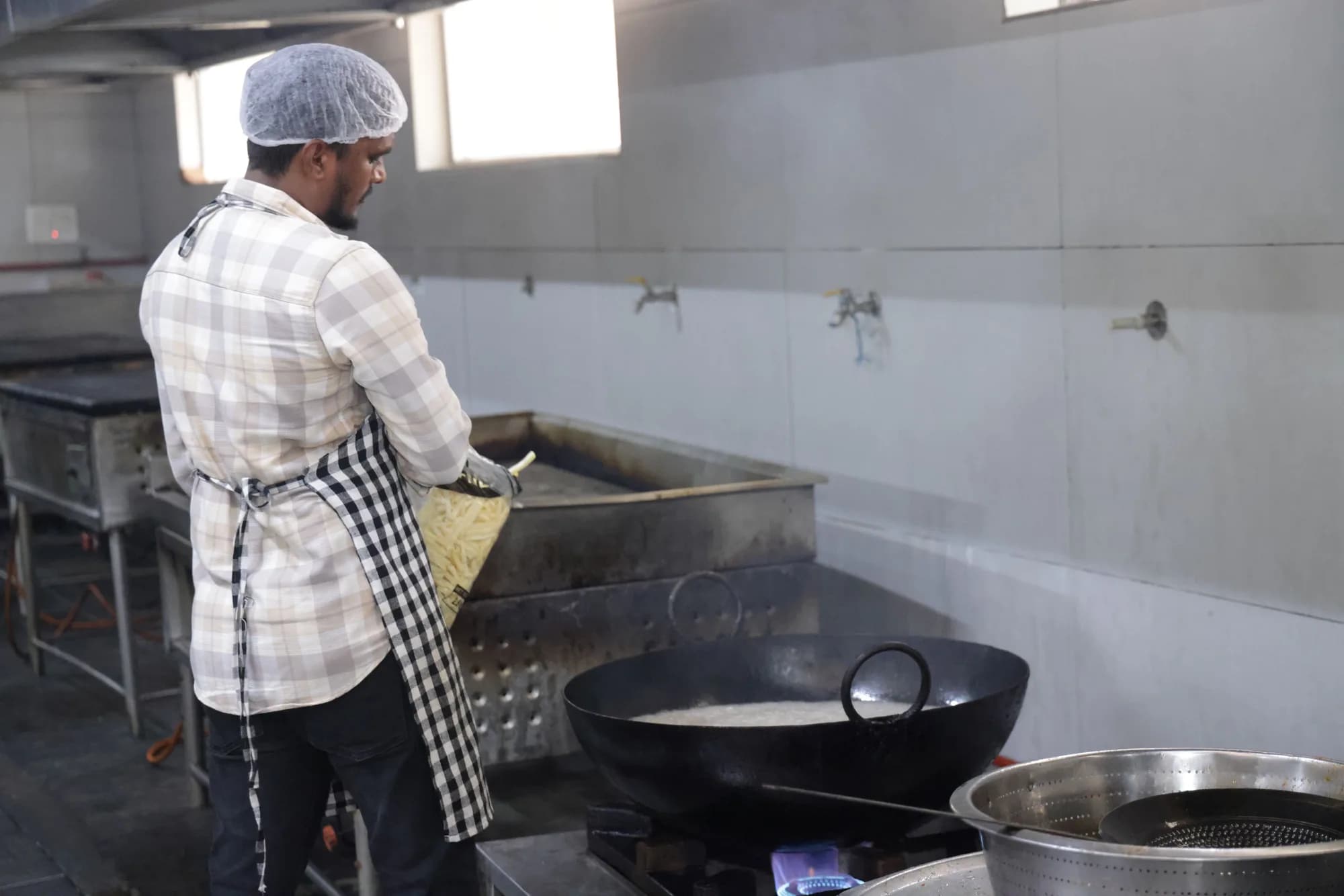 A cook in the PSSEMR School kitchen tipping chopped vegetables into a steel trough