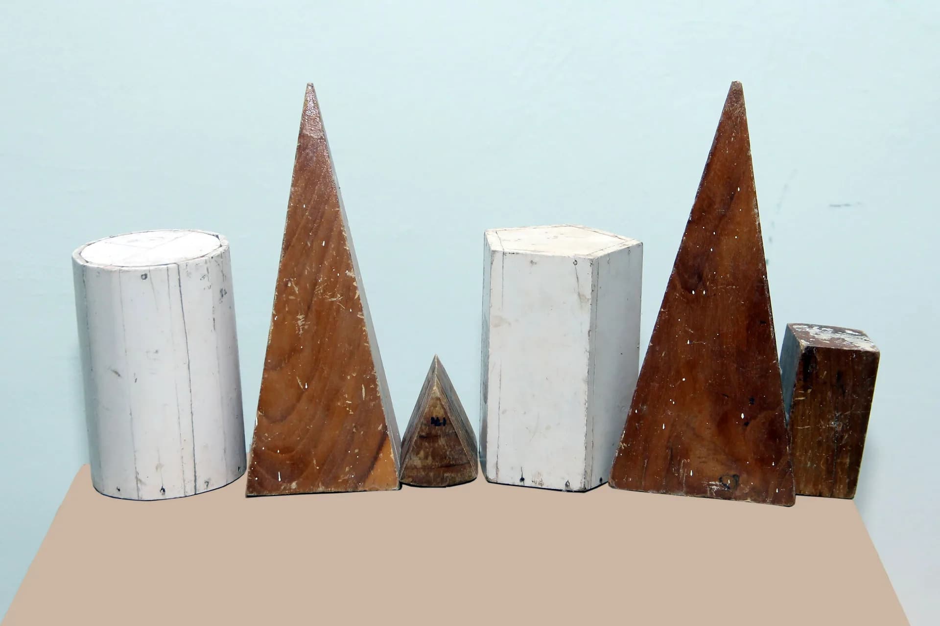 Six turned wooden geometric solids arranged on a shelf