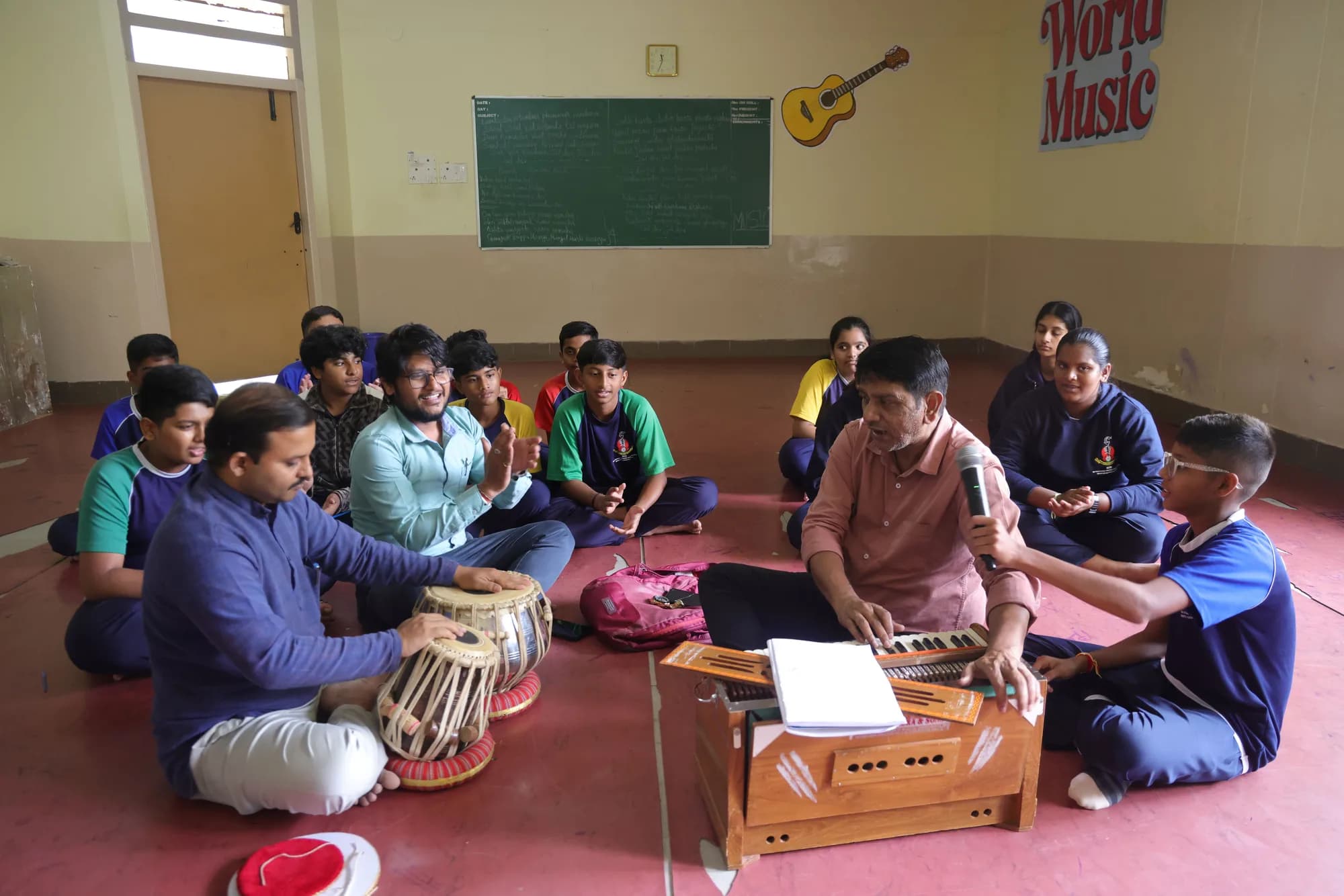 A music class seated on the floor at PSSEMR School, teachers at tabla and harmonium