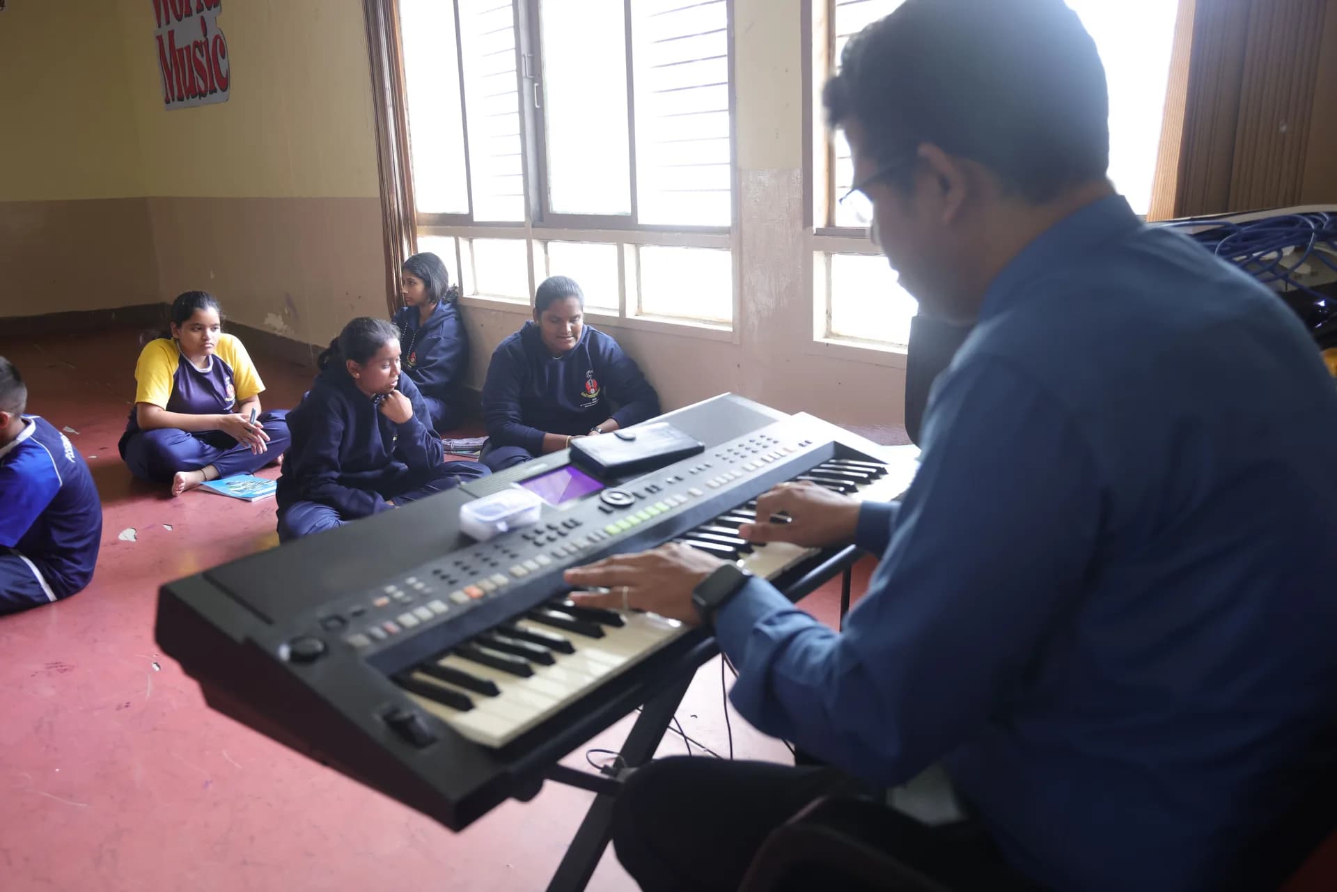 A teacher playing an electronic keyboard while pupils listen from the floor