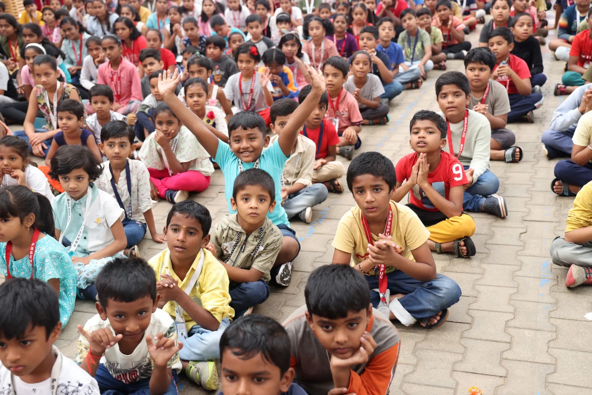 Young children seated cross-legged with hands raised at PSSEMR School