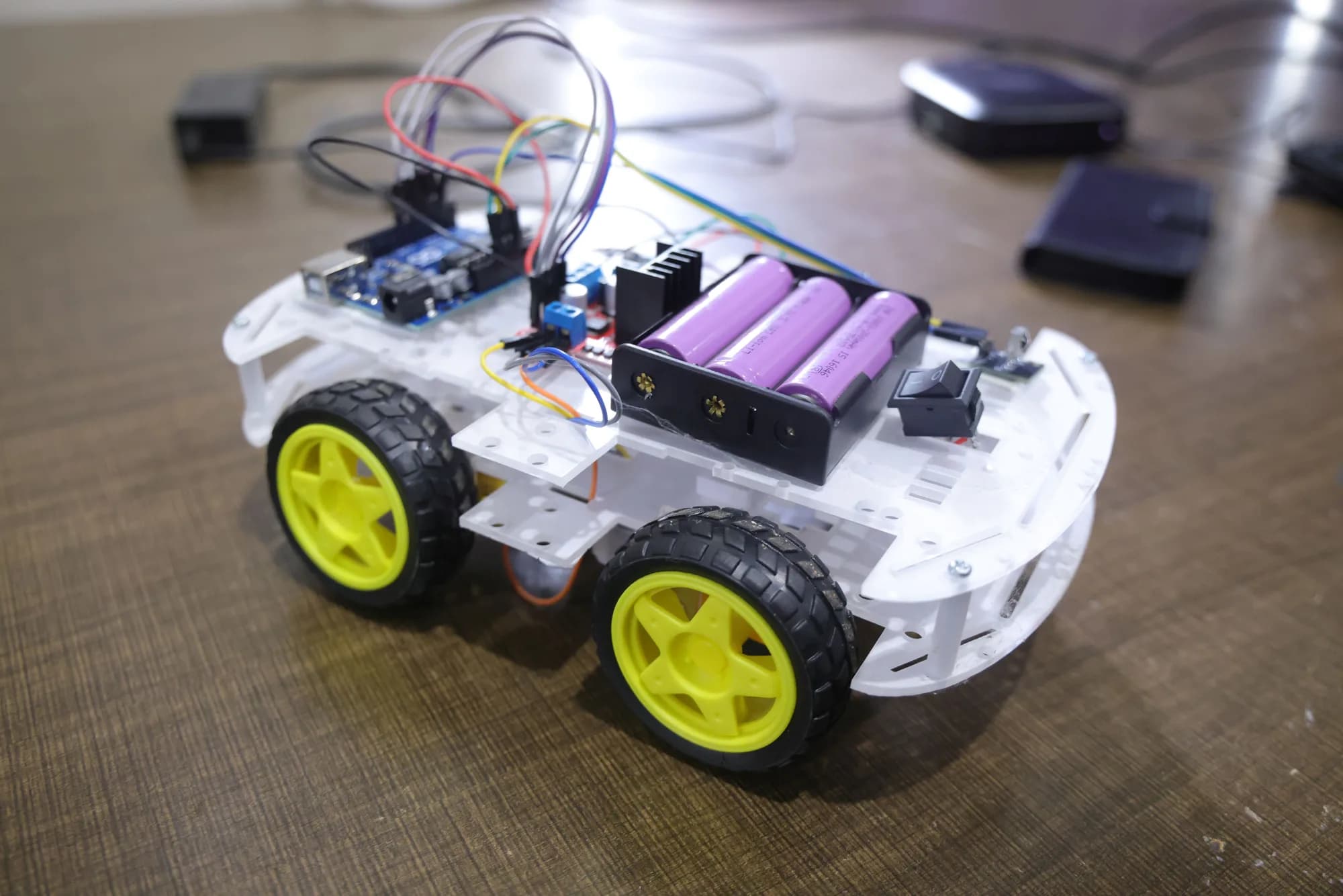 A four-wheel student-built robot with an Arduino board and battery pack on a bench