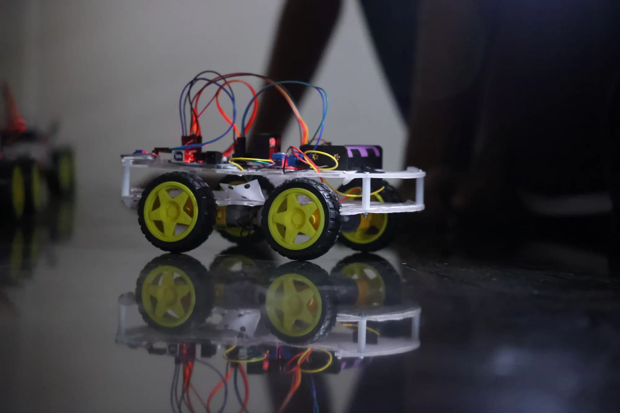 A student-built robot with its headlamp lit, reflected in a polished floor