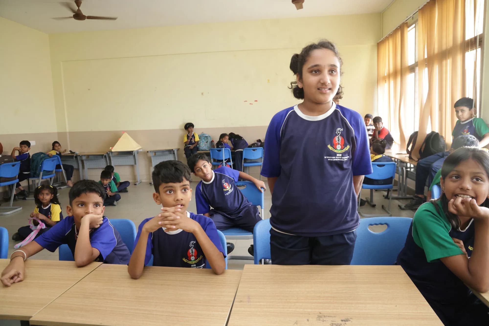 A girl speaking to her class at PSSEMR School while classmates listen from their desks