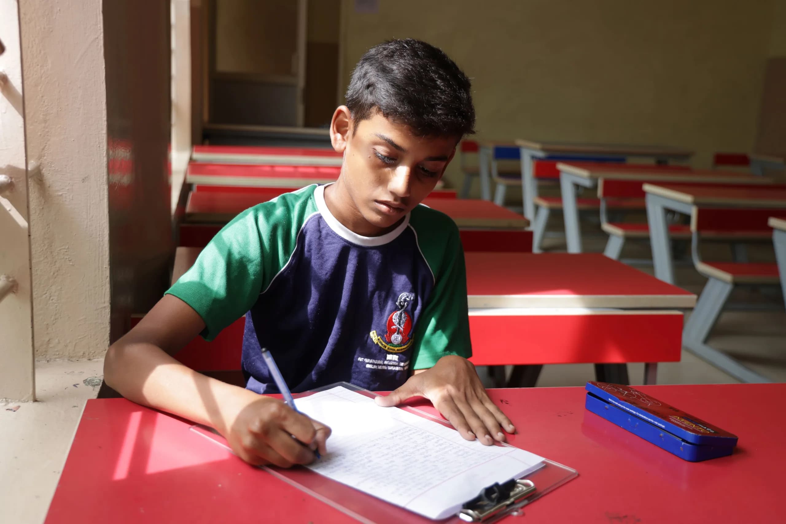A student writing at a desk during a written examination at PSSEMR School