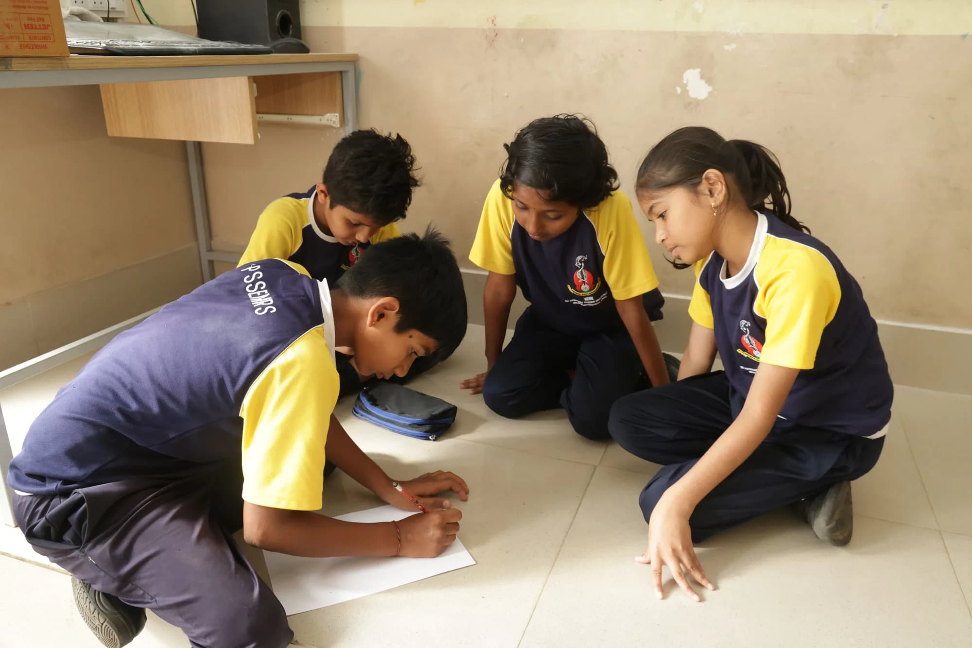 Four children working on one sheet of paper on a classroom floor at PSSEMR School
